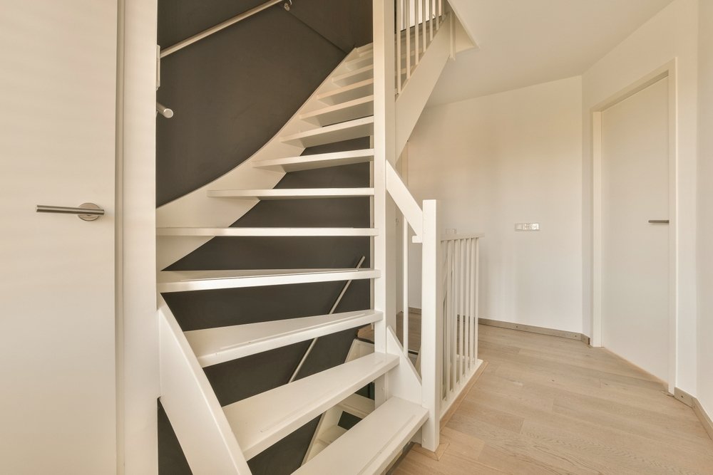 Een trapgat geschilderd in een levendige kleur, omgeven door een witte trapleuning en houten treden.