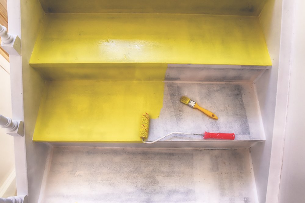 Een trap in een huis dat wordt geschilderd, met verfkwasten en verfblikken op de achtergrond.