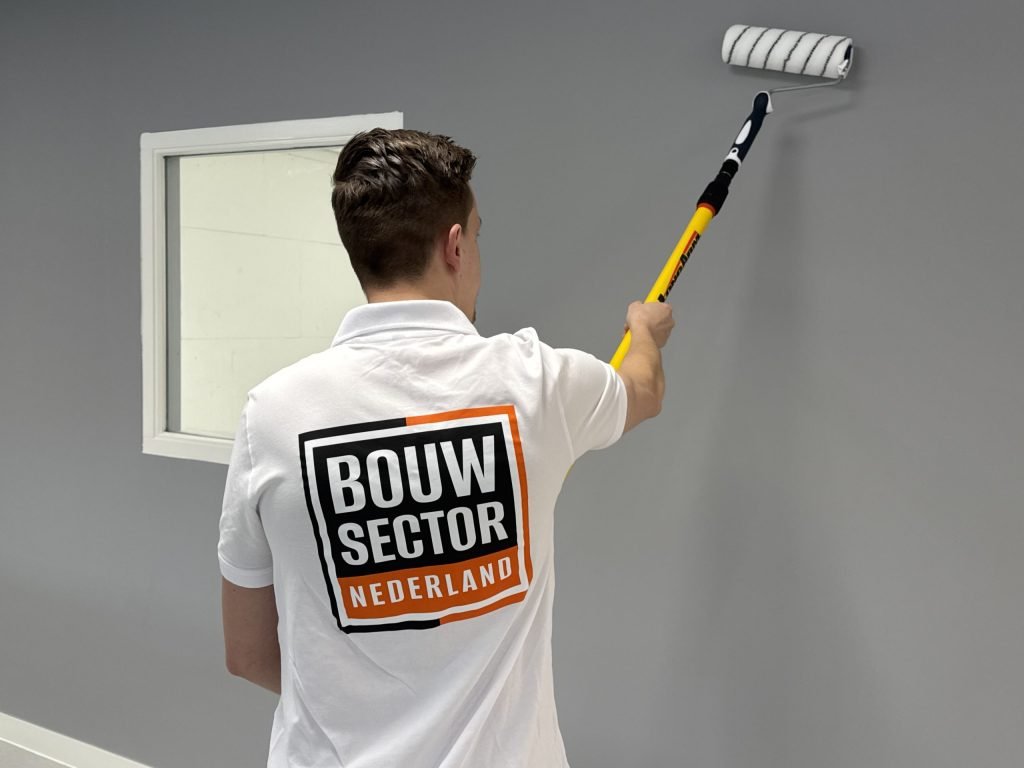 Schilder met het logo van Bouwsector Nederland op de rug rolt een muur in een grijze kleur